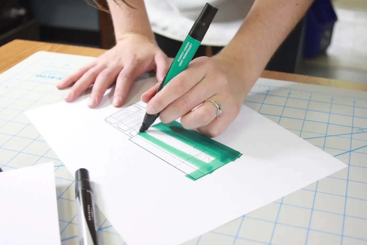 A designer sketching a website layout by hand on a cutting mat