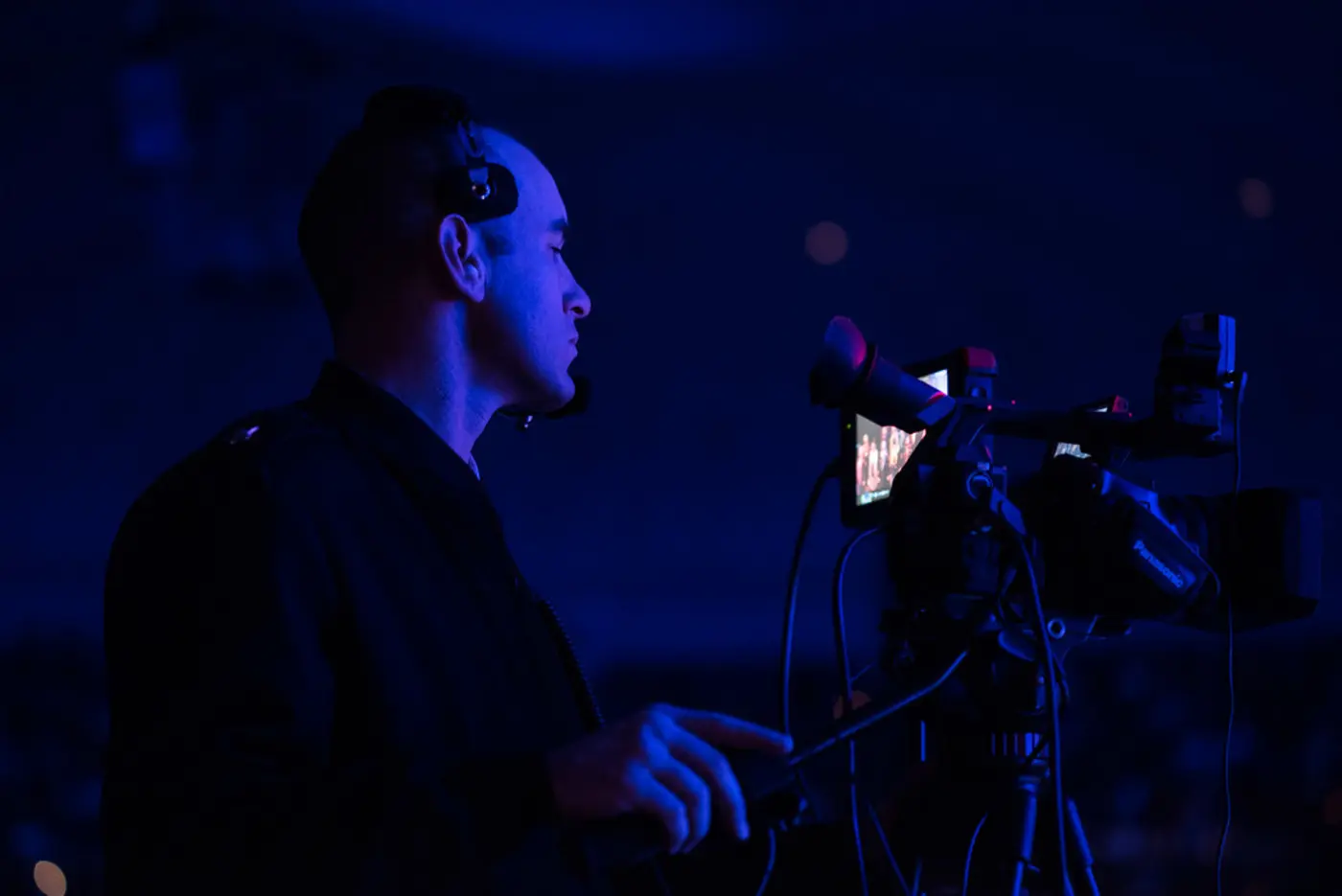 A camera operator filming with a professional video camera in blue stage light